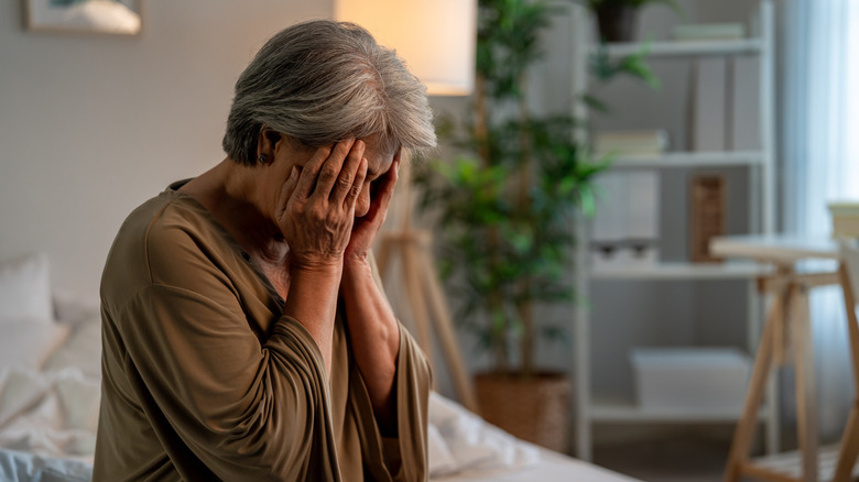 An upset retirement-age woman sitting on her bed