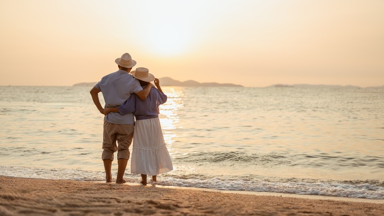 A couple standing on the beach at sunset, with the man holding the woman's hand