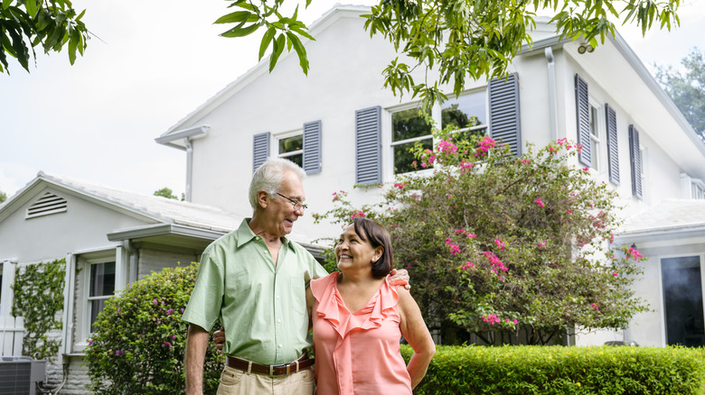 A mature couple looking into each other's eyes on the front lawn in front of a big house.