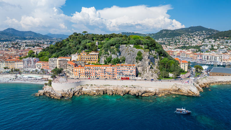 Aerial view of Nice's Castle Hill with lush greenery overlooking vibrant orange facades along Mediterranean coastline.