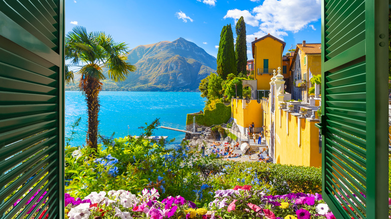 View through an open window with shutters looking down on the blue water and colorful picturesque resort village of Varenna, Italy, on the shores of Lake Como at summer.
