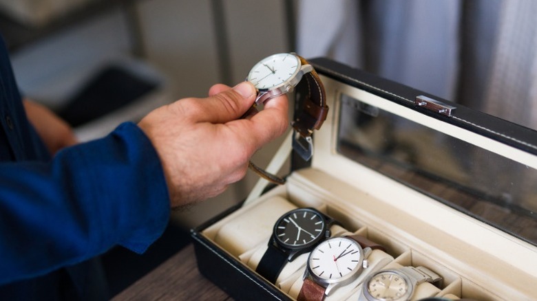 A man comparing different luxury watches sitting in a storage box on a table.