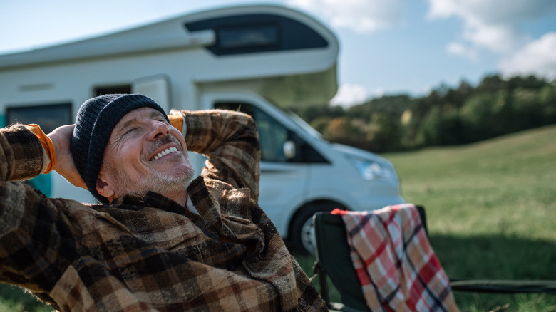 Happy man lounging in front of camper