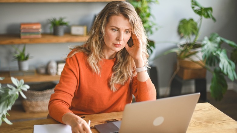A stressed-looking woman in front of a laptop at a desk