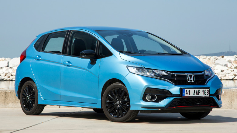 A blue Honda Fit parked outdoors near rocks with a blue sky in the background.