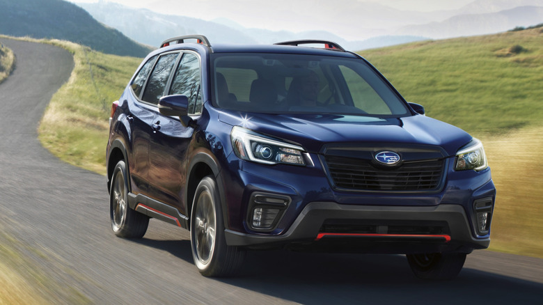 A dark blue Subaru Forester driving on a country road.