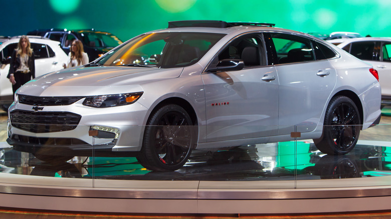 A white Chevy Malibu parked indoors at an auto show.