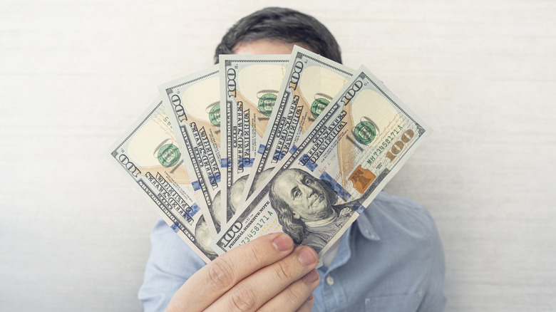 Man displays five $100 bills in front of his face like a fan