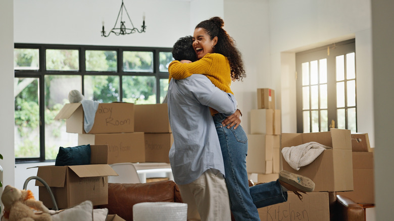 A couple hugging in a house with moving boxes stacked behind them