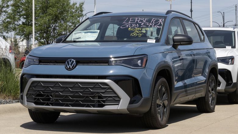 A blue 2026 Volkswagen Taos on display at a dealership with a lease price listed on the windshield.