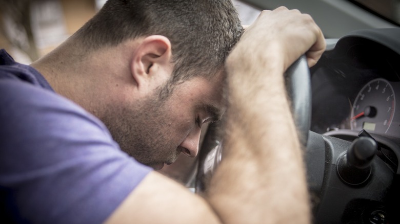 Driver leaning forward with his head down on a car steering wheel, appearing stressed