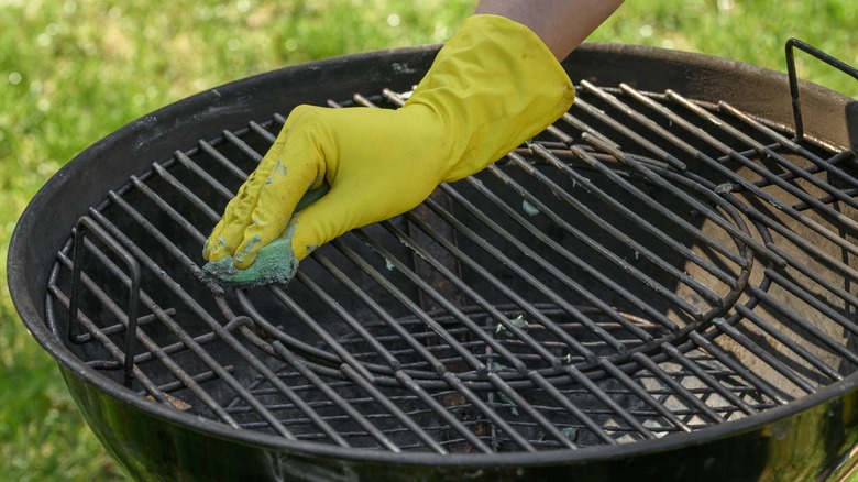 Gloved hand cleaning a charcoal grill with a sponge