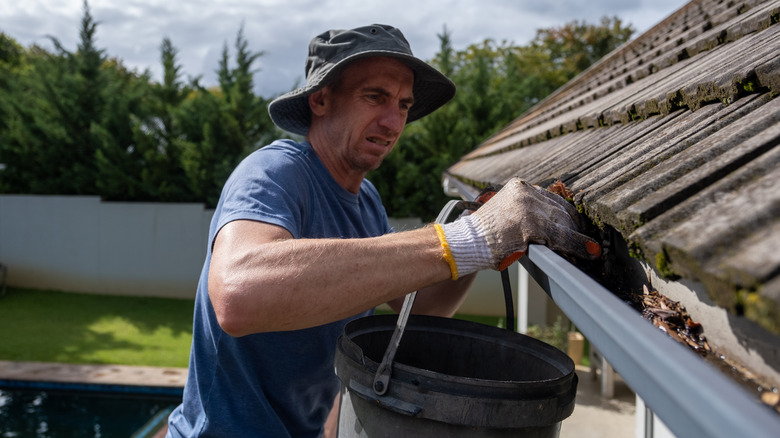 A man cleaning the gutters on his roof by hand.