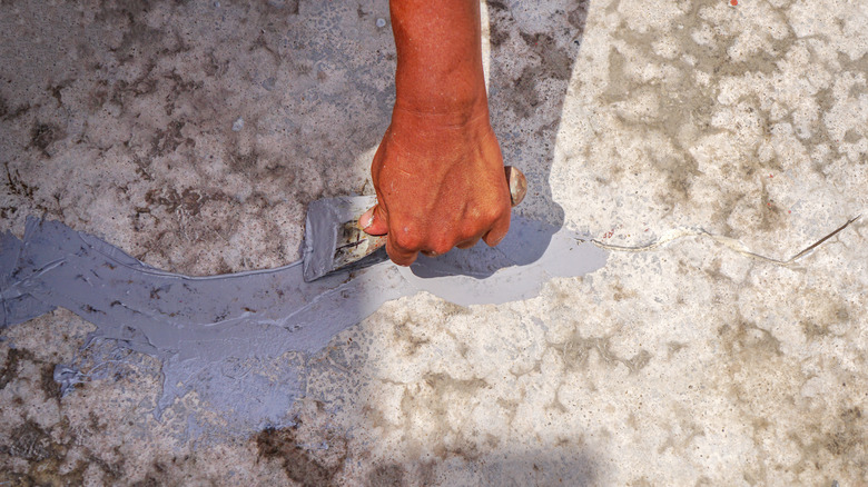 hand fixing a driveway crack