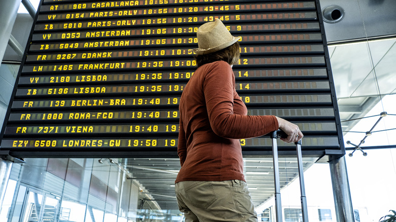 A person in the airport in front of the flight information display.