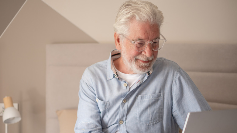 A senior man sitting on bed using laptop