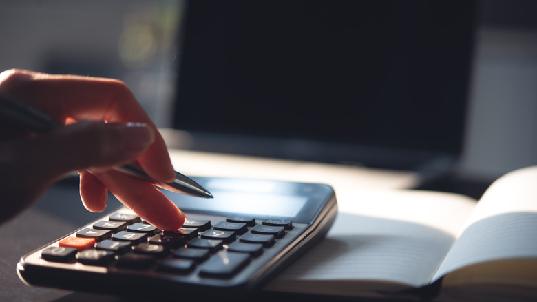 closeup of hand holding a pen and fingers pressing buttons on a calculator