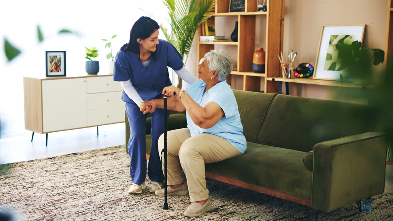 Woman with cane sitting on a couch while nurse assists her