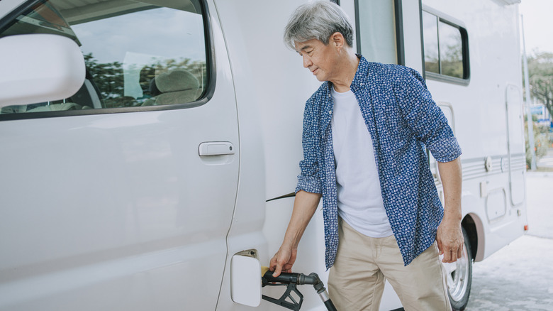 A mature man pumping gas into his RV camper at a gas station.