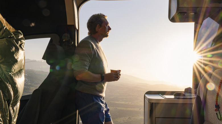A man watching the sunrise from the cabin of his RV with a cup of coffee.