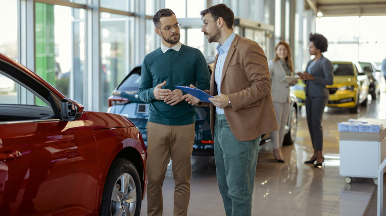 Car salespeople and customers on the sales floor of a car dealership.