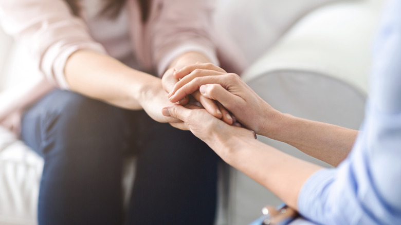 Woman comforting another women by holding her hands
