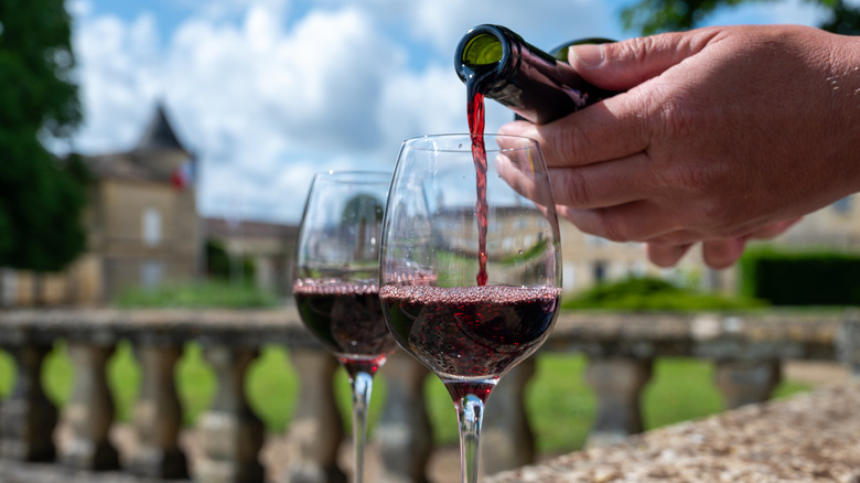Image of a hand serving red wine into two glasses