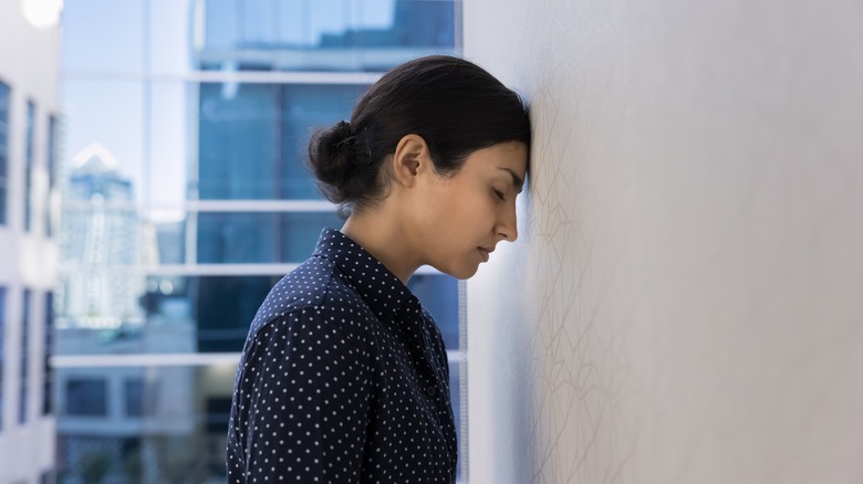 A stressed female employee with their head against wall