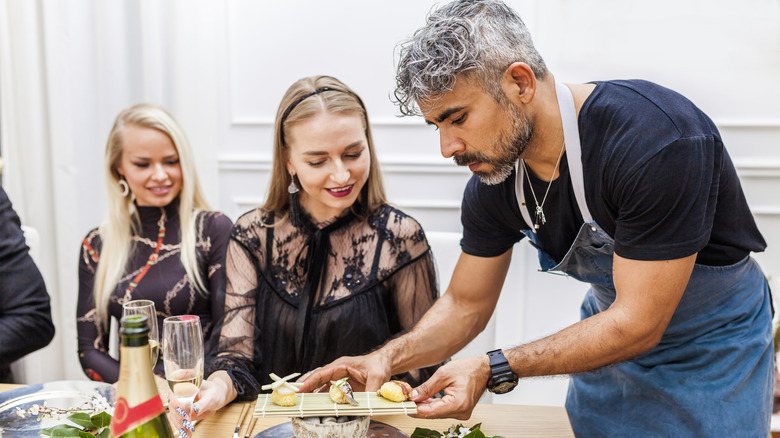Latin cook serving food to clients at table during private dinner at home.