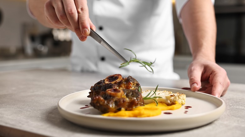 Professional chef serving dish at table indoors, closeup