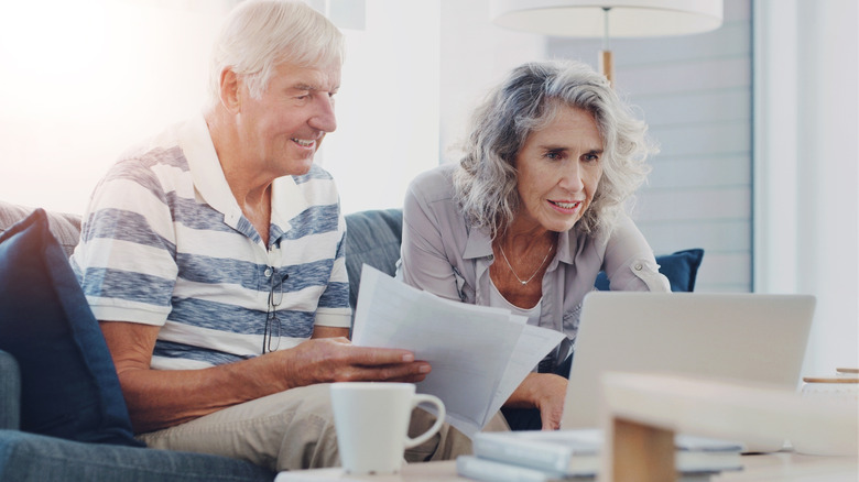 Older man and older woman looking a papers and laptop while on couch