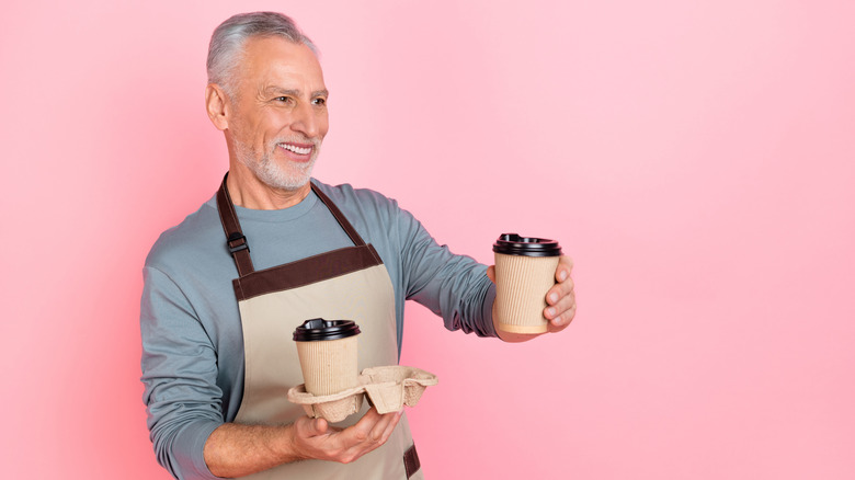 Older man in apron holding up togo cups