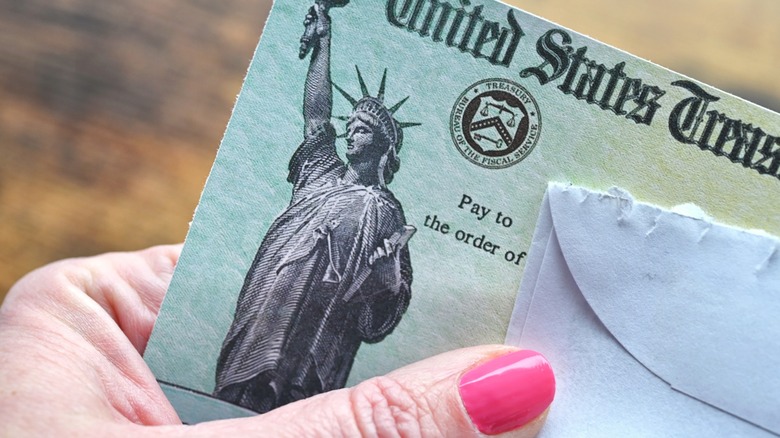 Close-up of a U.S. Treasury check being held next to an opened envelope