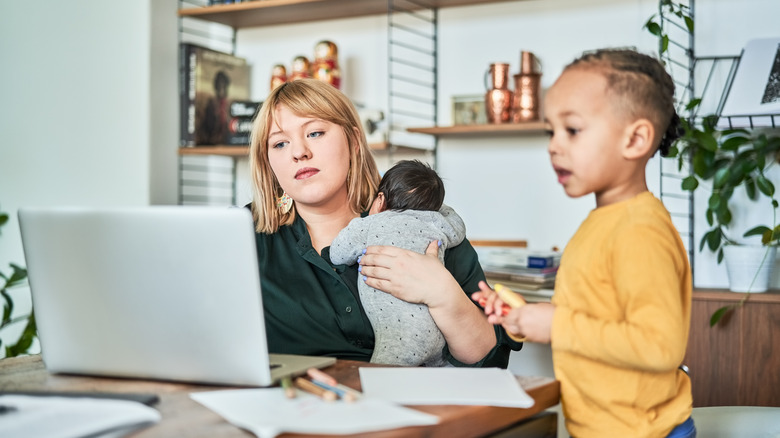 Woman working on laptop with children nearby
