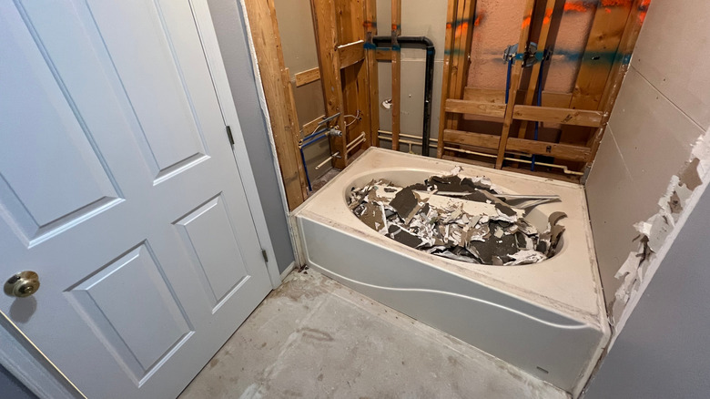 A bathtub filled with debris in a bathroom with exposed studs.