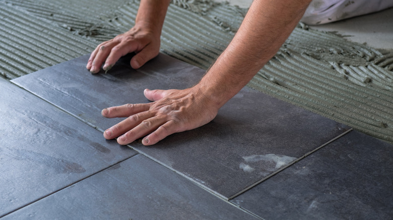 A close up of hands laying new tile on a floor.