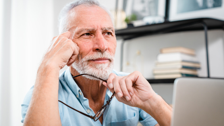A man in his 60s sitting at laptop and thinking