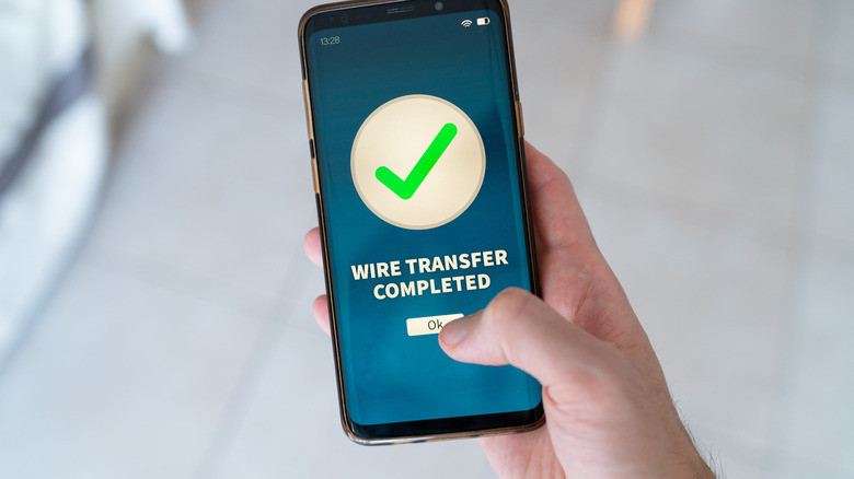 Hand holding smartphone reading 'wire transfer completed'