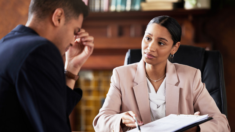 Woman in suit showing papers on a clipboard to a distressed-looking man