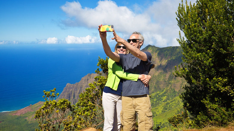 Senior couple taking a selfie atop a mountain in Hawaii with the ocean in the background
