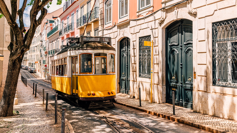 Trolley rolling down Lisbon street with cobblestone sidwalks