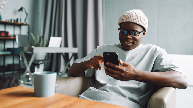 Young man with glasses and cap checks phone