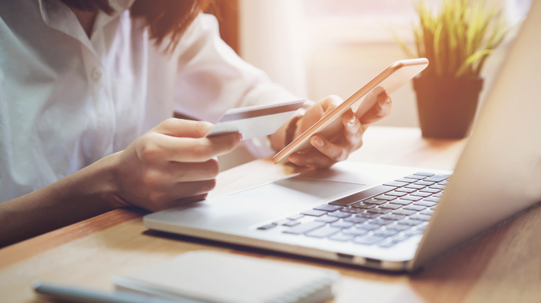 Woman holding credit card and phone in front of laptop