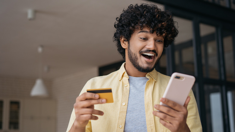 Young man smiling holding cell phone and credit card