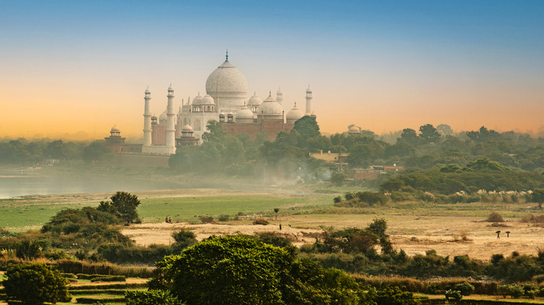 The Taj Mahal featuring its iconic domes dominates a lush landscape under a vibrant sunset.