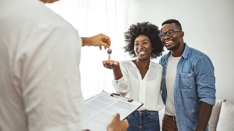 A couple being handed a set of keys by someone with a clipboard.
