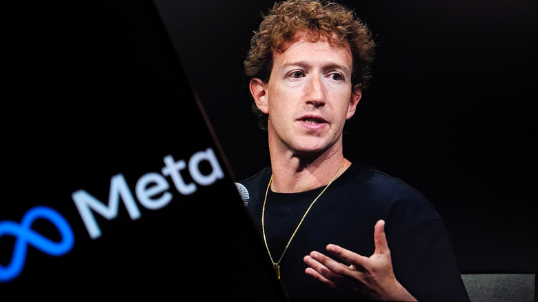 Mark Zuckerberg addresses a crowd from a dark podium, with a screen with the Meta logo just left of frame