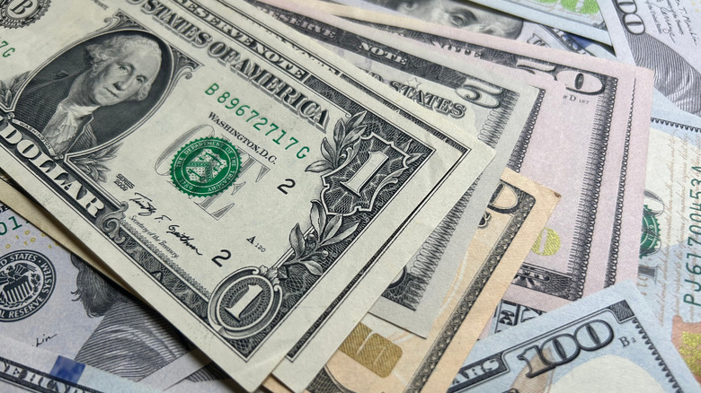 A $1 bill with a 2009 bill series stacked on top of a messy pile of larger bills