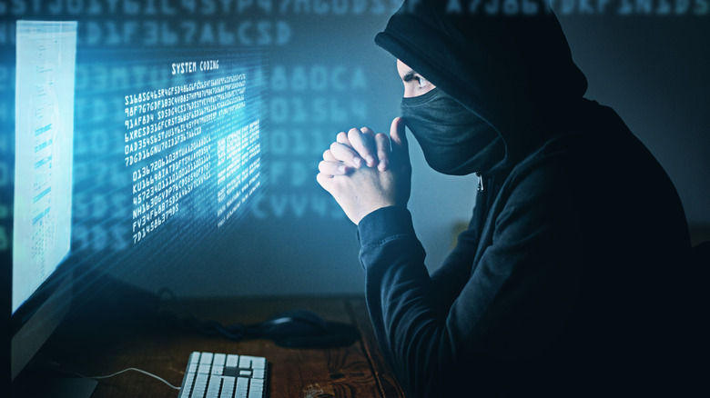Depiction of a masked hooded hacker looking at 'system coding" via a computer.