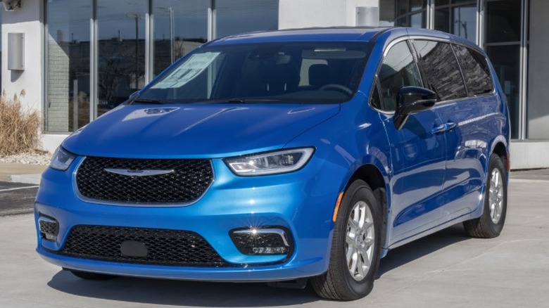 A new 2020s-era blue Chrysler Pacifica parked in front of a building in the sun.